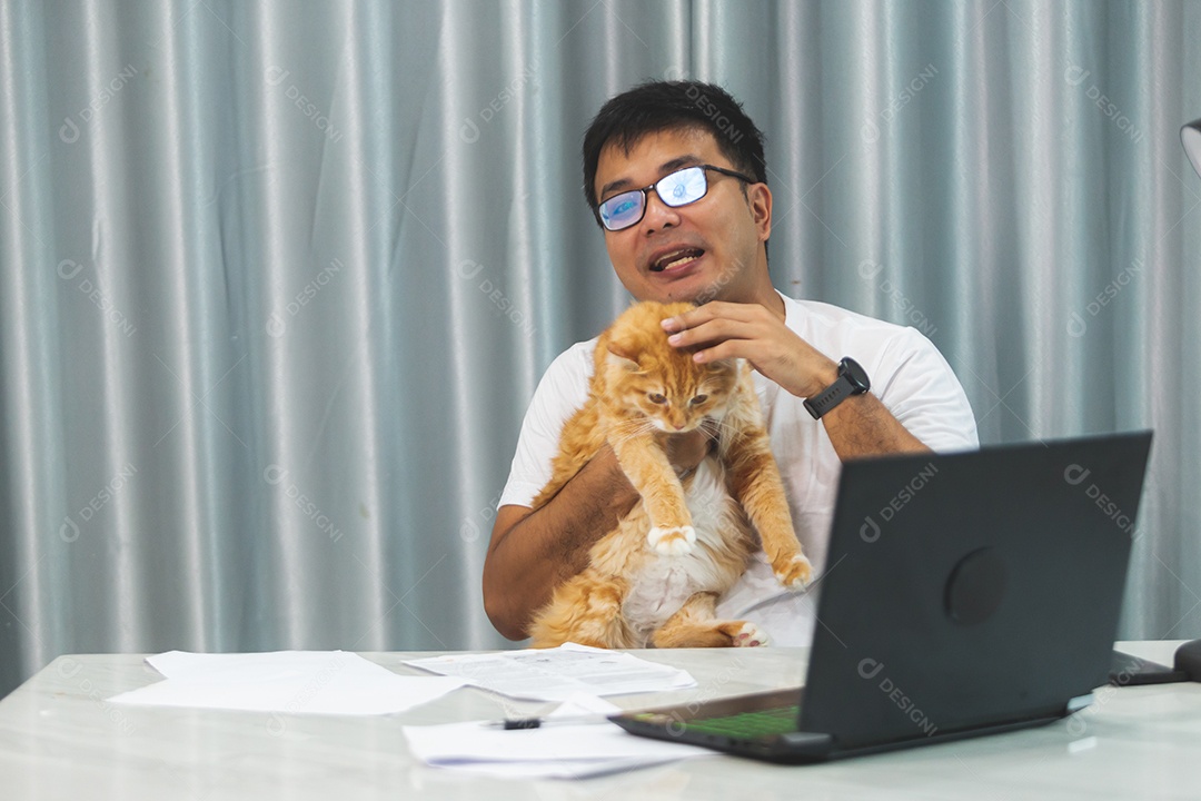Homem segurando seu gato de estimação sobre escritório mexendo notebook