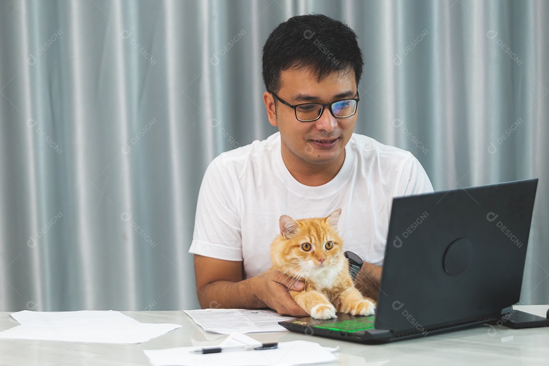 Homem segurando seu gato de estimação sobre escritório mexendo notebook