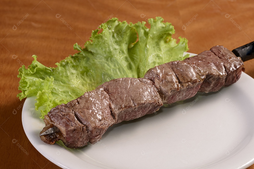 Churrasco de carne em espetos. Quibe brasileiro tradicional em chapa branca na mesa de madeira.