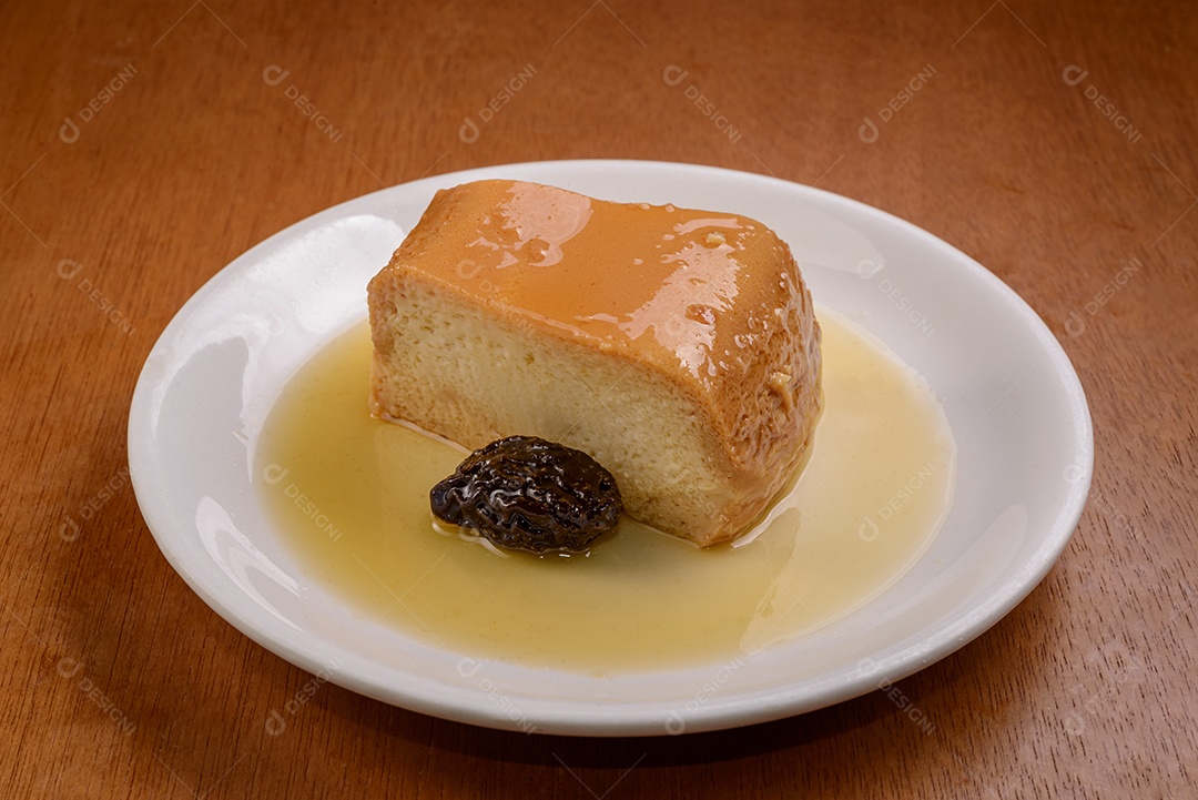 Pudim de leite com calda de ameixa em chapa branca na mesa de madeira.