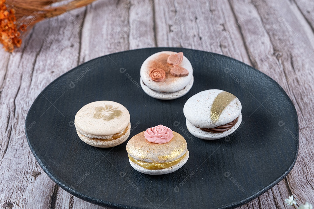 Quatro macarons, decorados com tinta comestível e fondant, em um prato preto.