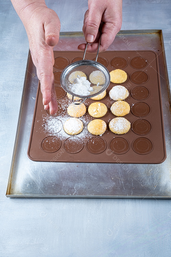 Confeiteiro polvilhando açúcar sobre guloseimas de casamento em uma placa de silicone marrom.