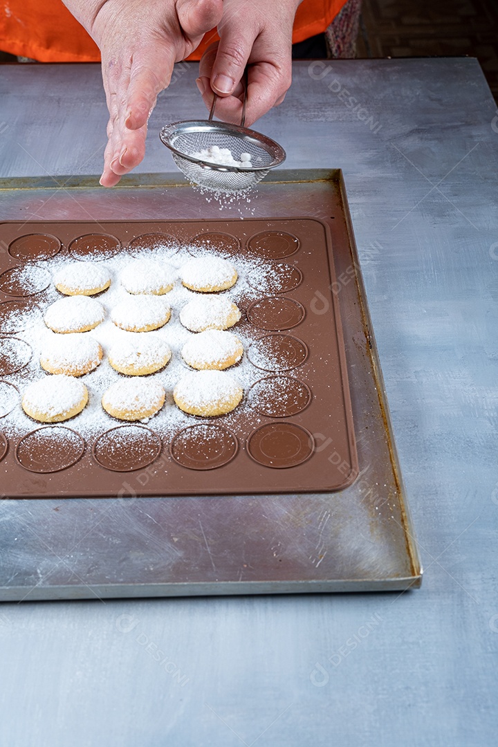Confeiteiro polvilhando açúcar sobre guloseimas de casamento em uma placa de silicone marrom.