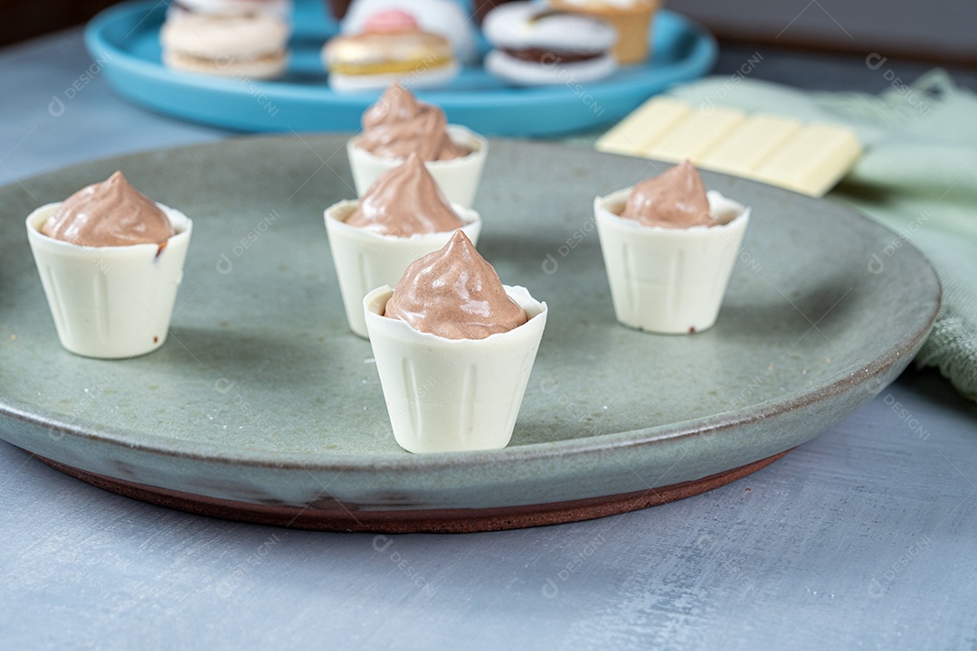 Confeiteira enchendo copinhos de chocolate branco com mousse de chocolate ao leite.