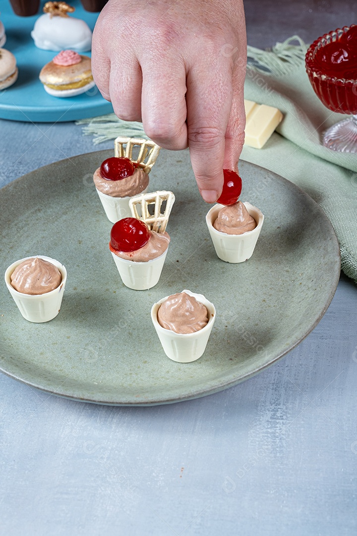 Confeiteira enchendo copinhos de chocolate branco com mousse de chocolate ao leite.