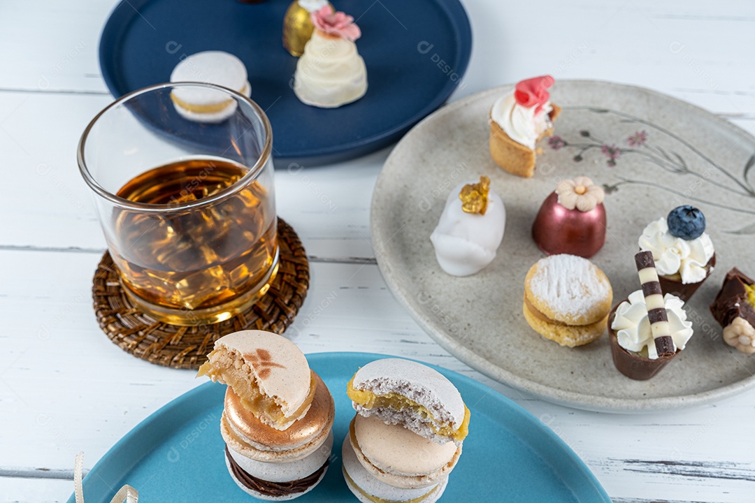 Macarons empilhados cercados por um copo de uísque gelado e doces de casamento extravagantes.