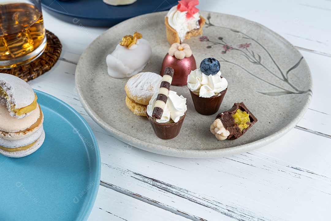 Macarons empilhados cercados por um copo de uísque gelado e doces de casamento extravagantes.