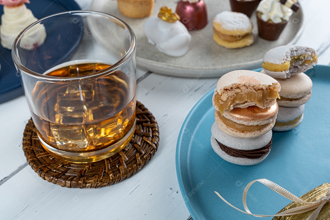 Copo de uísque com gelo cercado por uma vista sortida de sobremesas de casamento.