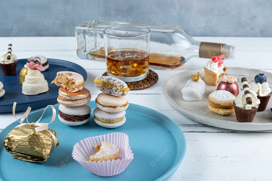 Copo de uísque com gelo cercado por uma vista sortida de sobremesas de casamento.