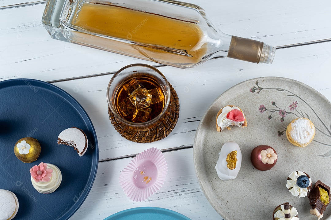 Copo de uísque com gelo cercado por uma vista sortida de sobremesas de casamento.