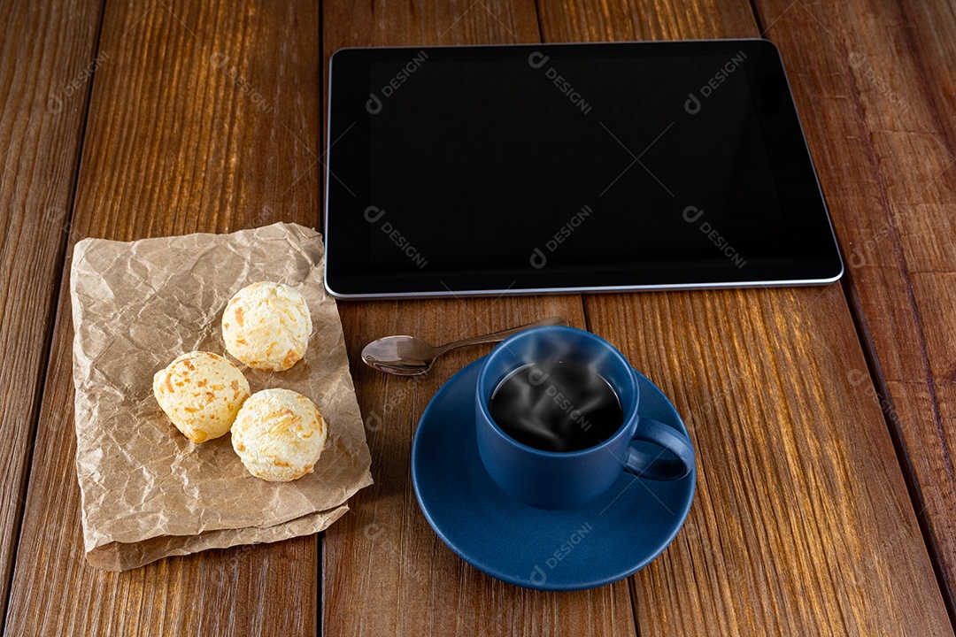 Pães de queijo ao lado de xícara de café, colher de cobre e tablet_vertical.