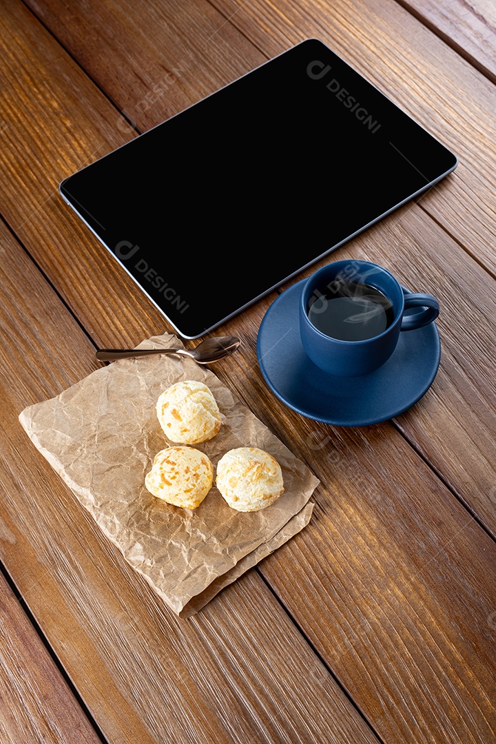 Pães de queijo ao lado de xícara de café, colher de cobre e tablet_vertical.