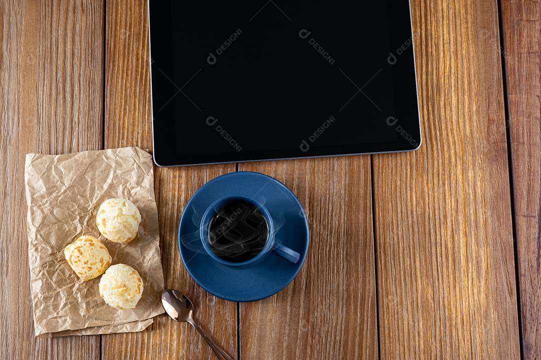 Pães de queijo ao lado de xícara de café, colher de cobre e tablet_vertical.