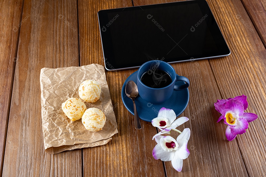 Pães de queijo ao lado de xícara de café, colher de cobre e tablet_vertical.