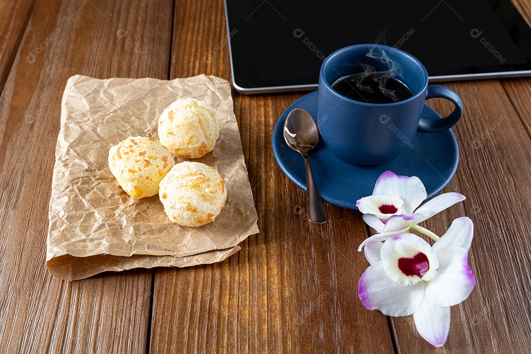 Pães de queijo ao lado de xícara de café, colher de cobre e tablet_vertical.