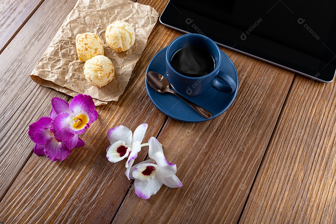 Pães de queijo ao lado de xícara de café, colher de cobre e tablet_vertical.