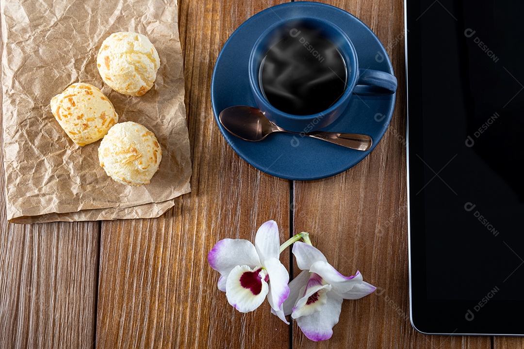 Pães de queijo ao lado de xícara de café, colher de cobre e tablet_vertical.