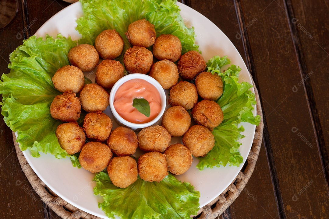 Prato de coxinhas fritas sobre prato branco mesa madeira