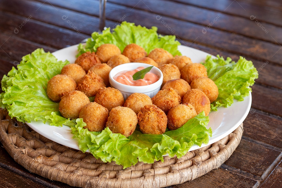 Prato de coxinhas fritas sobre prato branco mesa madeira