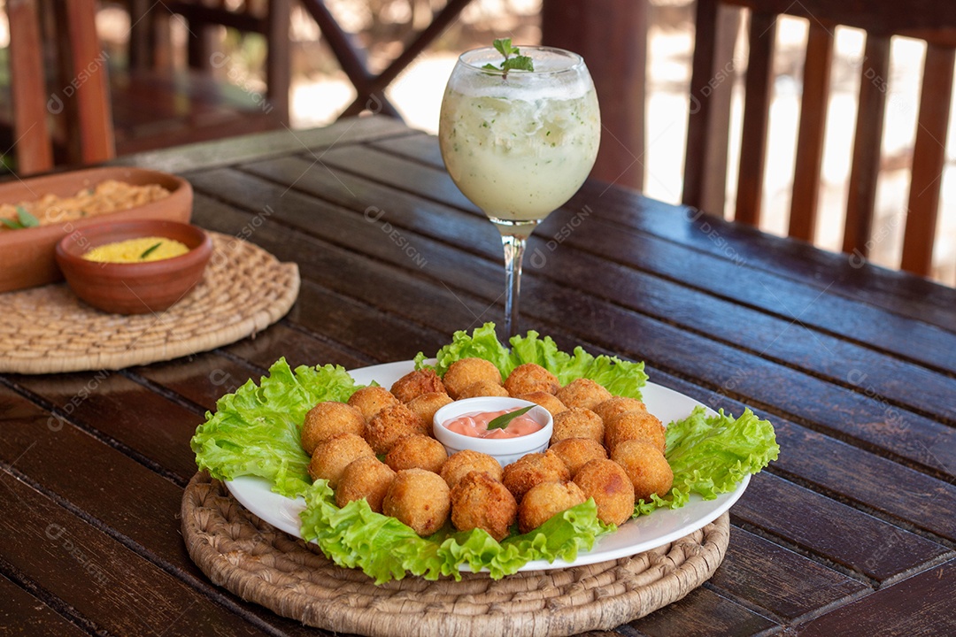 Prato de coxinhas fritas sobre prato branco mesa madeira