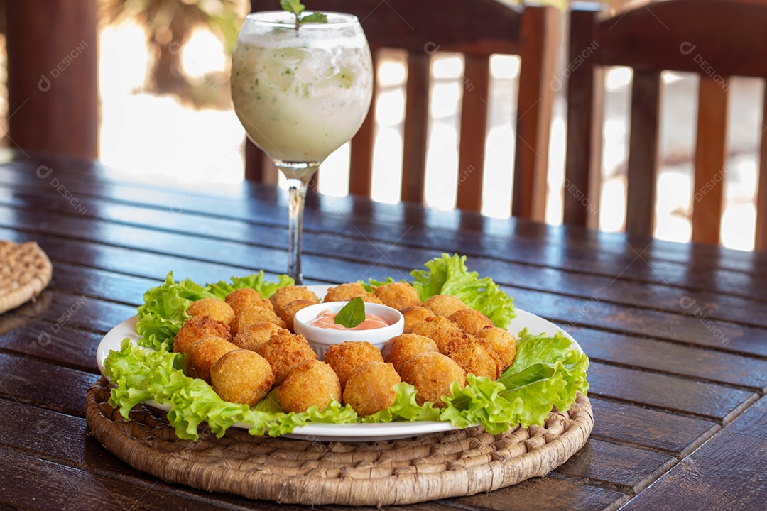Prato de coxinhas fritas sobre prato branco mesa madeira