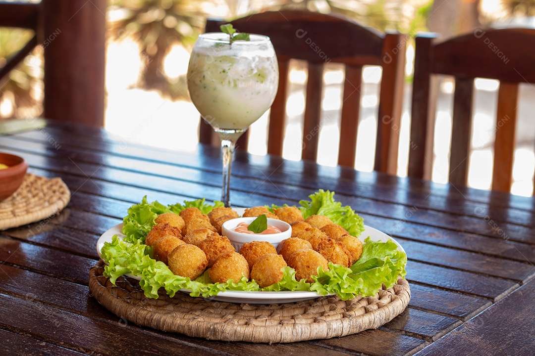 Prato de coxinhas fritas sobre prato branco mesa madeira