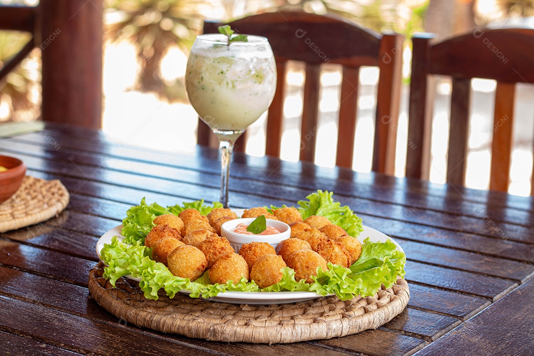 Prato de coxinhas fritas bebida sobre taça de vidro sobre prato branco mesa madeira