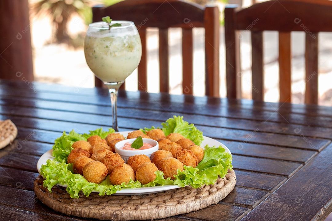 Prato de coxinhas fritas bebida sobre taça de vidro sobre prato branco mesa madeira