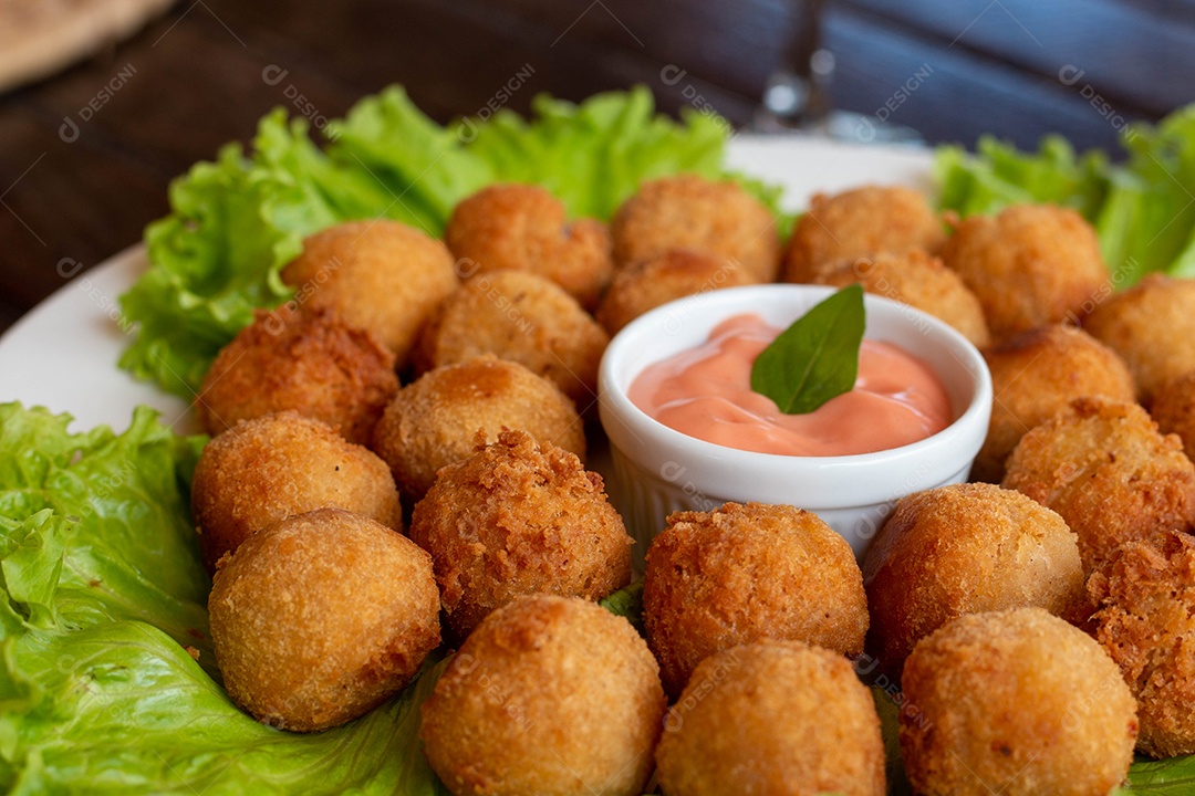 Prato de coxinhas fritas bebida sobre taça de vidro sobre prato branco mesa madeira