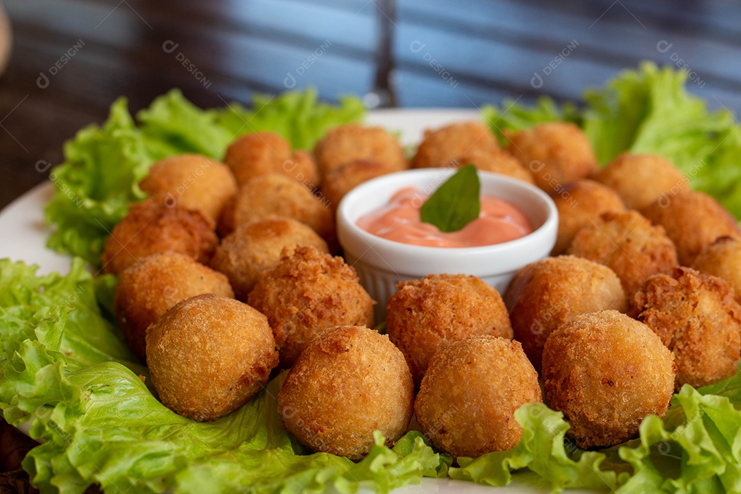 Prato de coxinhas fritas sobre prato branco mesa madeira