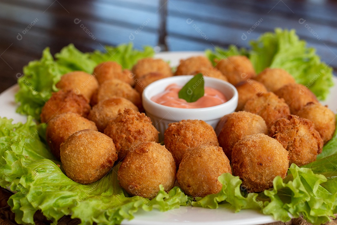 Prato de coxinhas fritas sobre prato branco mesa madeira