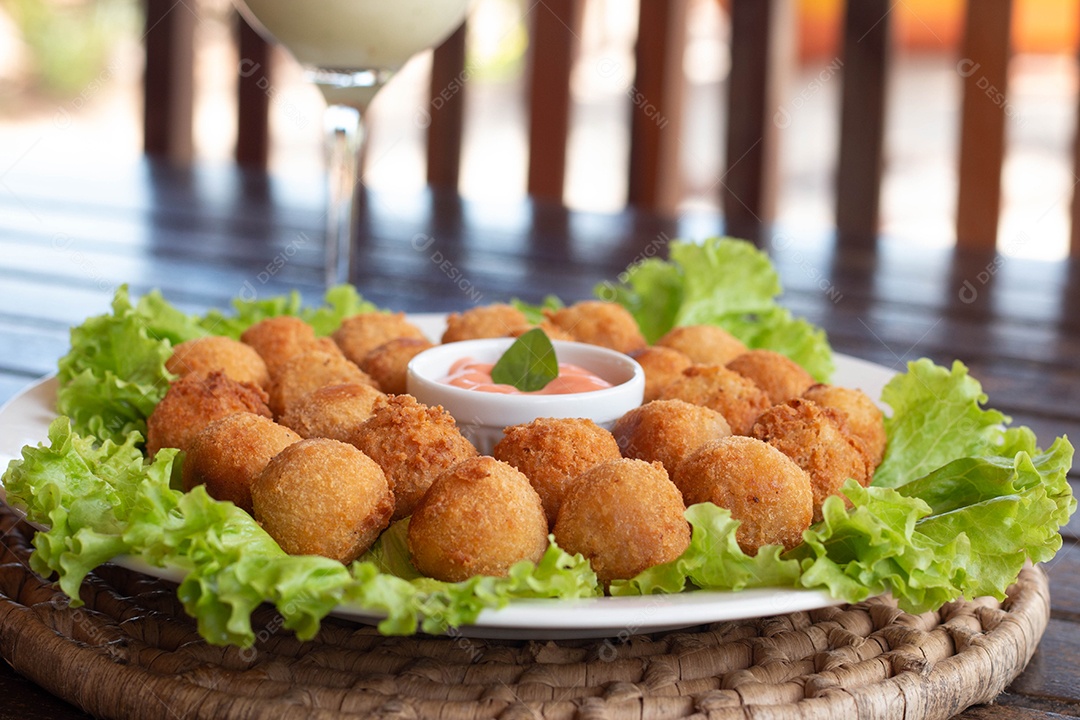 Prato de coxinhas fritas sobre prato branco mesa madeira