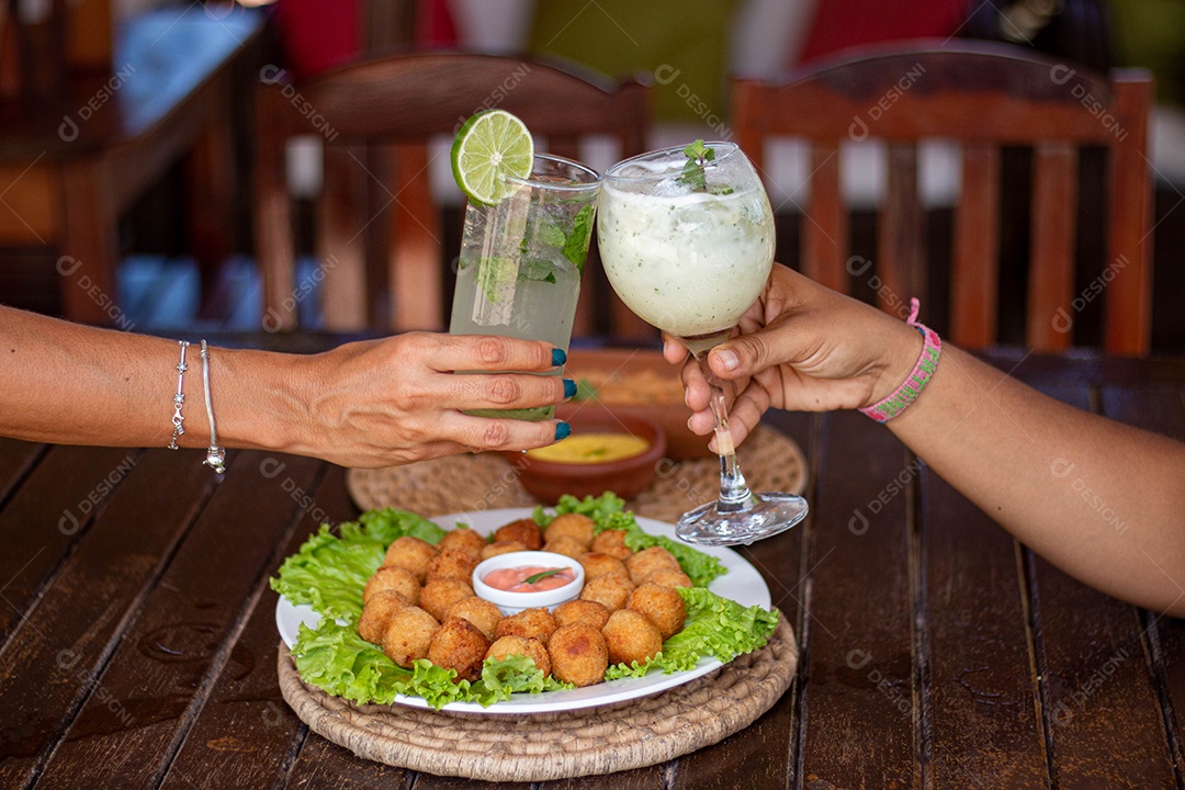 Pessoas brindando bebida sobre um restaurante e mesa coxinhas fritas