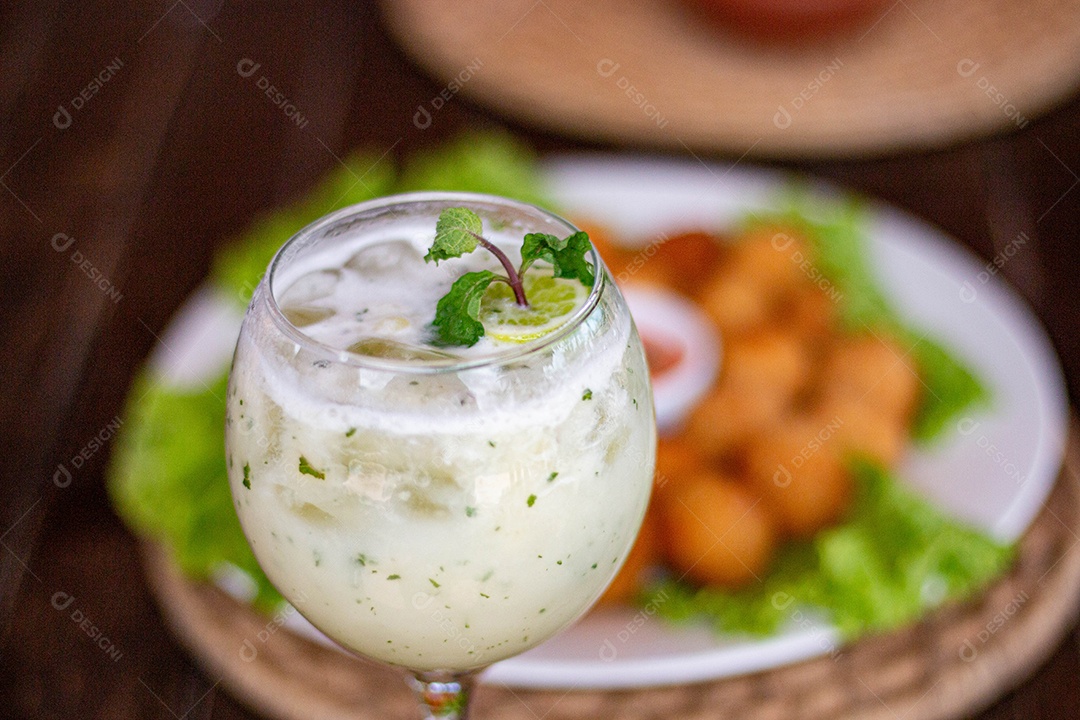 Prato de coxinhas fritas bebida sobre taça de vidro sobre prato branco mesa madeira