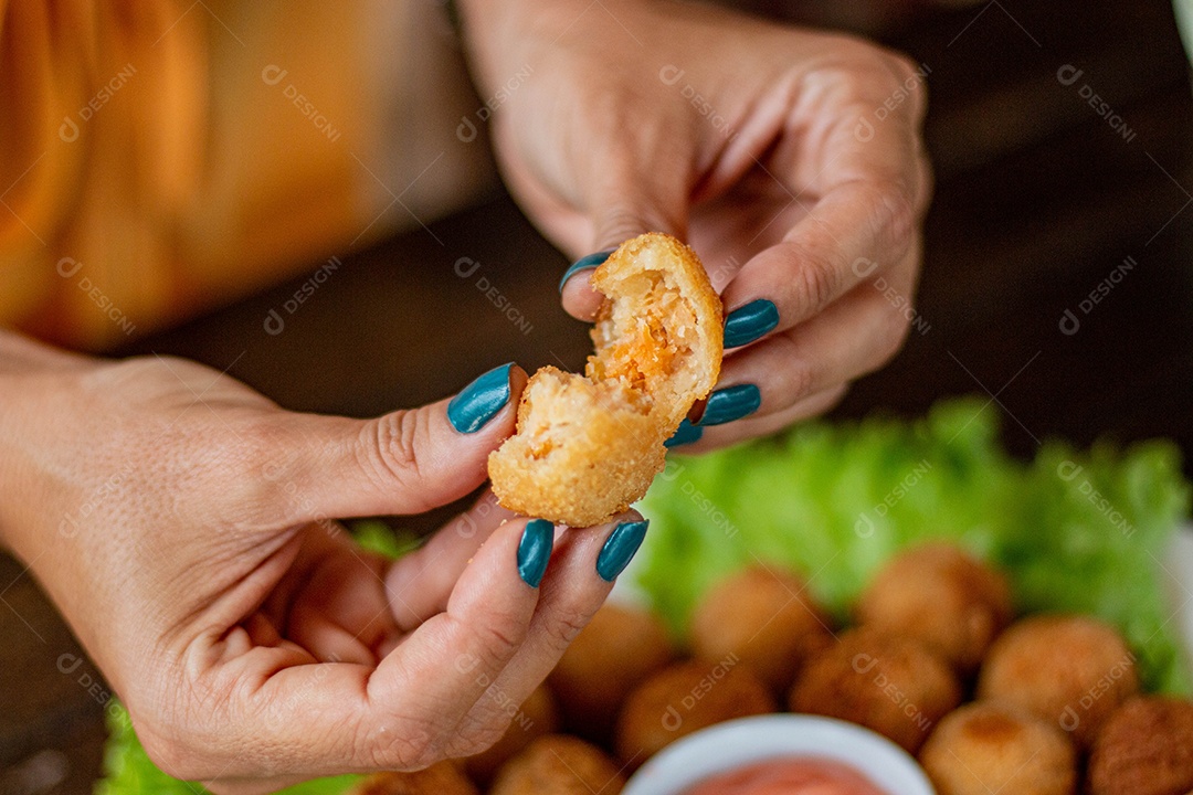 Mãos de pessoa segurando coxinha pequena frita