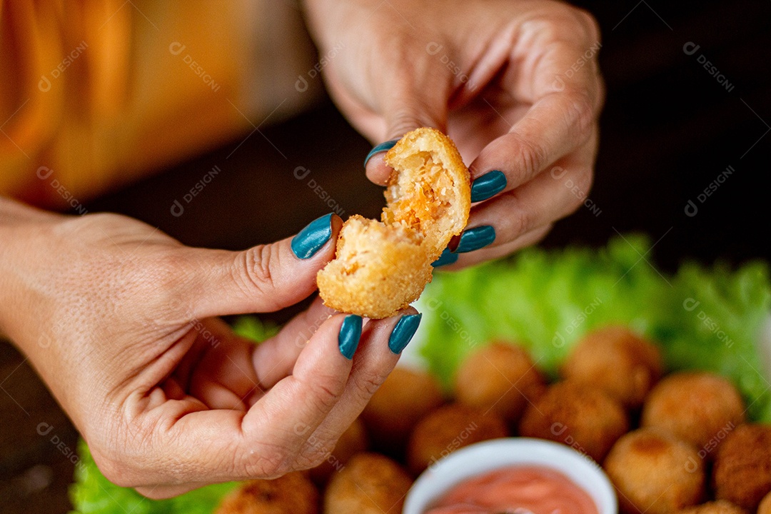 Mãos de pessoa segurando coxinha pequena frita