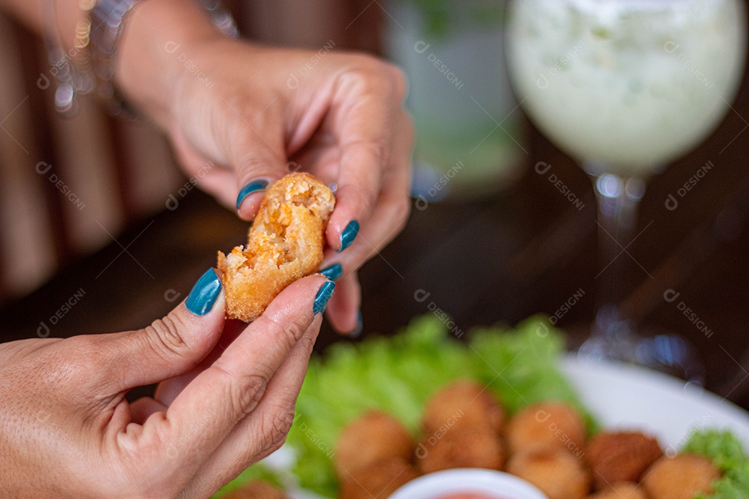 Mãos de pessoa segurando coxinha pequena frita