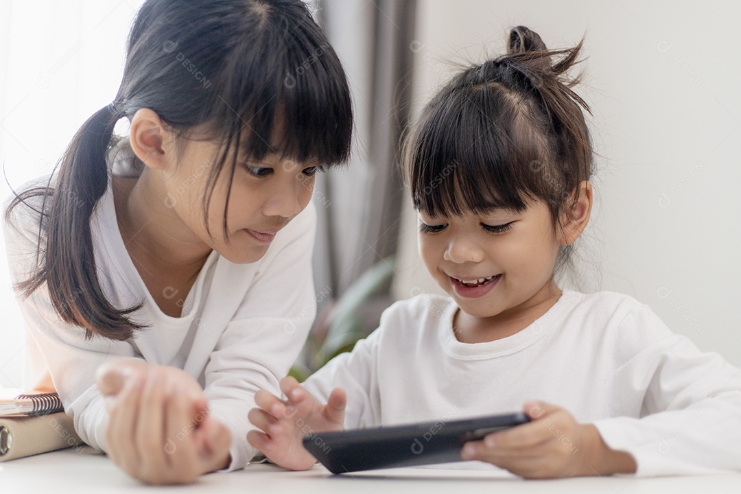 Garota asiática se divertindo em casa, usando smartphone e rindo, jogando videogame em um telefone celular. conceito de crianças e gadgets