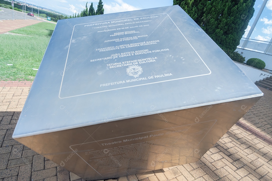 Placa de metal com memorial no Teatro municipal de Paulínia em um dia nublado.