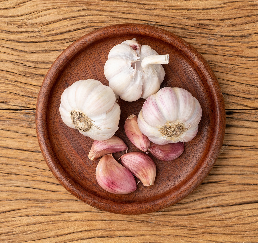 Bulbo de alho e cravo em um prato sobre a mesa de madeira.