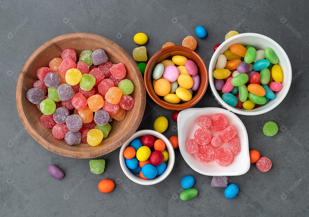 Doces coloridos sortidos em tigelas sobre fundo de pedra.