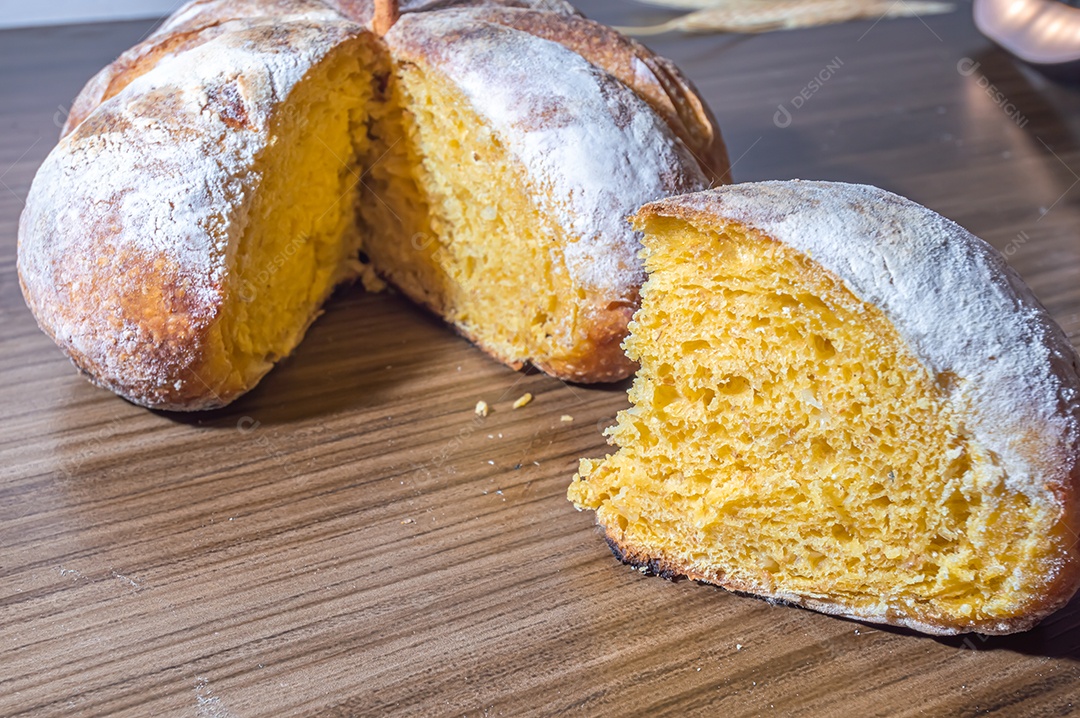 Pão de abóbora feito em forma de abóbora em uma mesa de madeira.