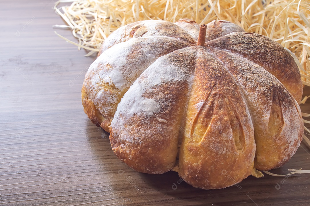 Pão de abóbora feito em forma de abóbora em uma mesa de madeira.