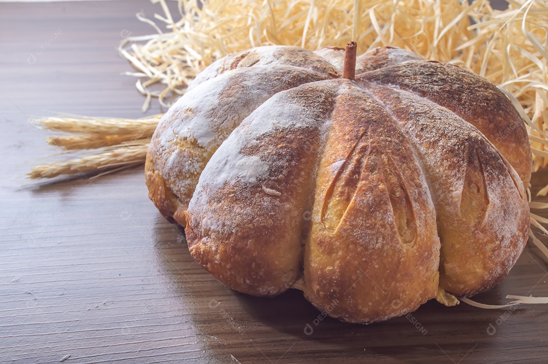 Pão de abóbora feito em forma de abóbora em uma mesa de madeira.