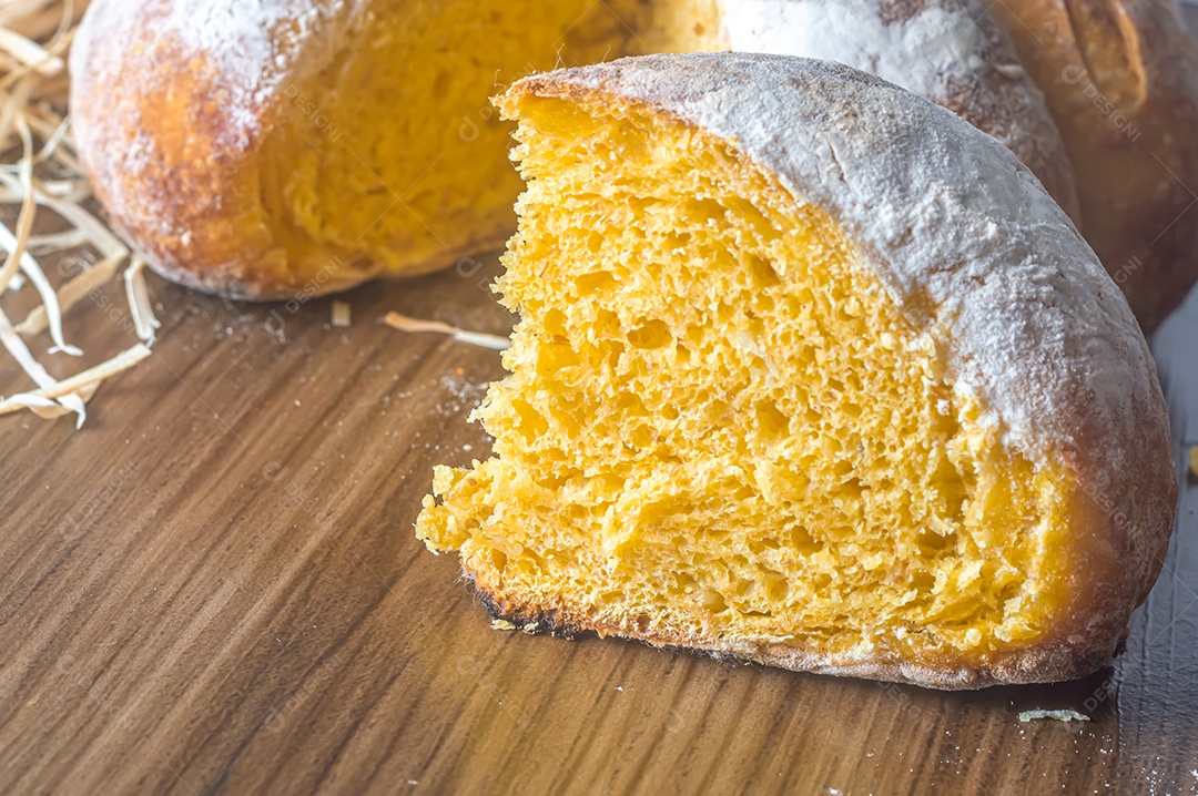 Pão de abóbora feito em forma de abóbora em uma mesa de madeira.