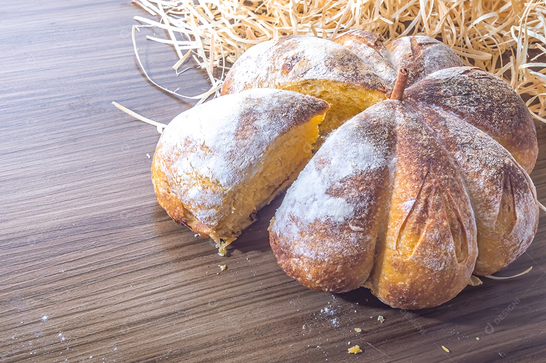 Pão de abóbora feito em forma de abóbora em uma mesa de madeira.