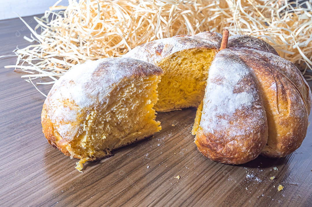 Pão de abóbora feito em forma de abóbora em uma mesa de madeira.