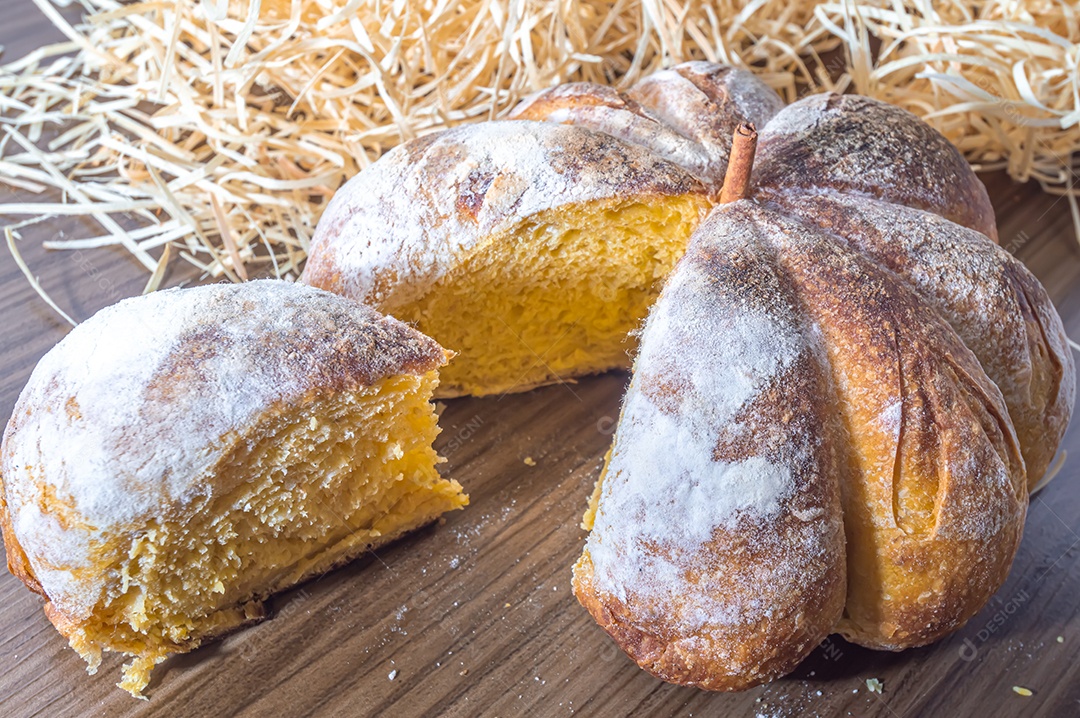 Pão de abóbora feito em forma de abóbora em uma mesa de madeira.