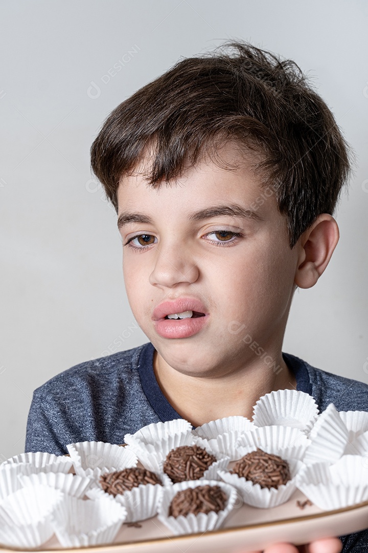 Criança de 9 anos segurando uma bandeja com balas de chocolate e fazendo cara de que não quero mais comer.