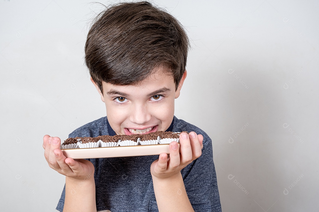 Menino de 9 anos mostrando os dentes e segurando uma bandeja com várias bolas de chocolate brasileiras.